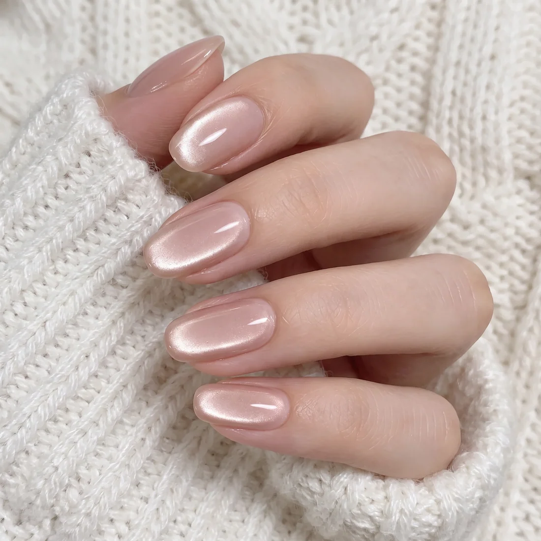 Pearl-pink cat-eye gel nails resting on a cream knit sweater sleeve